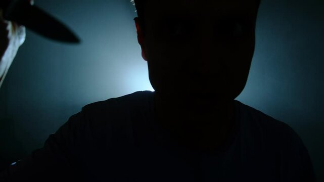 Silhouette of man with knife in darkness.
