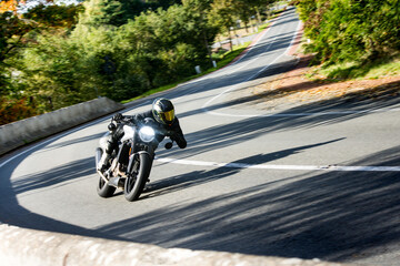 A skilled motorcyclist leans into a sharp turn on a scenic, tree-lined road, showcasing speed and...