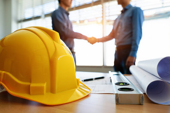 Two construction professionals shaking hands over blueprints and safety helmet