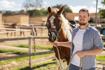 Young man leading horse by bridle in paddock