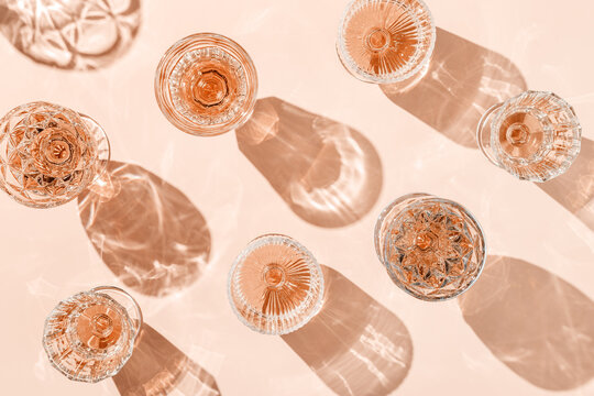 Minimal pattern of Top view glasses of rose wine or champagne on soft pink background, artistic shadows and sun glare. Aesthetic still life crystal wineglass, sparkling drinks for summer party