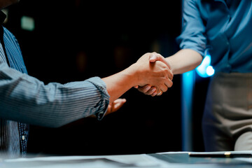 Portrait of cooperation between businessman and woman in office at night. Teamwork handshake.