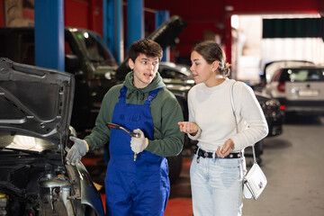 Auto mechanic checking young woman client car in car service center