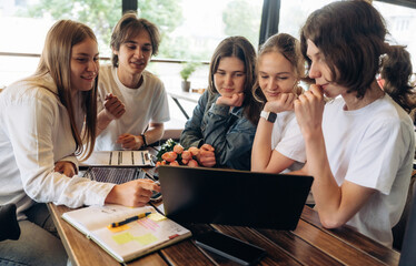 Laptop and documents are on the table. Group of young friends are in the cafe restaurant