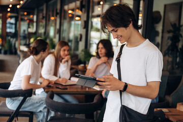 Guy is holding digital tablet. Group of young friends are in the cafe restaurant
