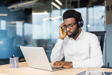 A man wearing headphones and glasses rests while listening to music with his eyes closed at his desk