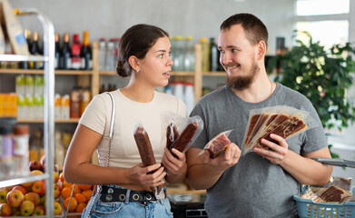 Married couple looking at hamon and dried sausage in store. Market visitor choose consider dried...