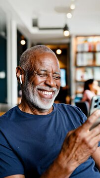 Smiling senior man enjoying a cheerful video call on his smartphone in a modern caf&eacute;, wearing wireless earbuds, relaxing alone. Generative AI
