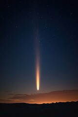 Bright comet with glowing tail streaking across starry night sky over dark silhouetted landscape with warm horizon glow