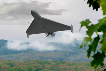 A military drone in flight over a green forest against a cloudy sky