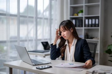 Stressed asian businesswoman having headache while working on laptop in office