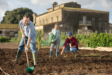 Farmer with a shovel drips a garden to plant seeds. Man with his family works on a farm and...