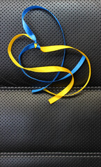 A symbolic heart made of yellow and blue ribbons in the colors of the Ukrainian flag on a black leather background. Vertical image with colored ribbons