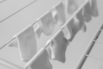 Close-up of white baby socks hanging on a drying rack indoors, monochrome image with soft light and shallow depth of field, concept of childhood and domestic care