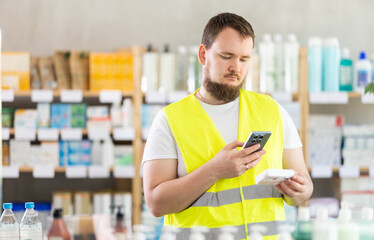 Young man builder in uniform scanning qr code for box of paracetamol tablets in pharmacy