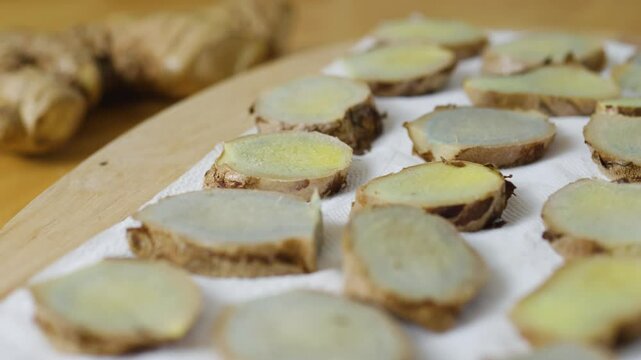 Thinly sliced ginger root drying on a white paper towel, resting atop a wooden cutting board, offers a flavorful ingredient for cooking or a natural remedy for wellness