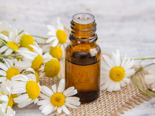 A small glass bottle with chamomile essential oil on an old wooden background.