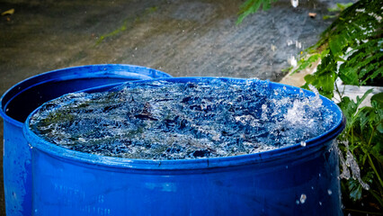 Rain water dropping into a blue drum wide shot