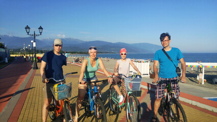 Group of four people family are riding bikes on a sidewalk near sea and mountains in Sochi