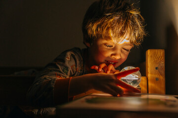 boy lies in his bed in pajamas and looks at the night light with the planet saturn before going to...