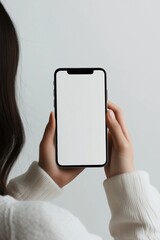 Person holding smartphone with blank screen in hands against light background