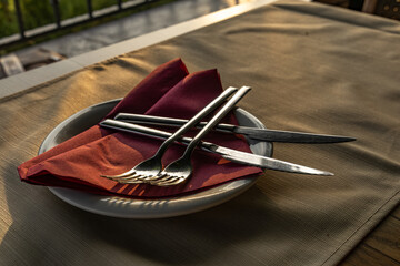 Cutlery, knives, forks arranged on an elegant burgundy napkin on a plate in a restaurant,