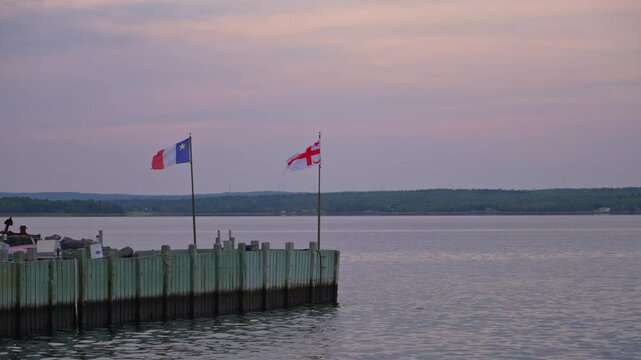 Sunrise over harbor with Acadian and Mikmaq flags waving gently