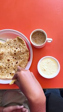 4K Vertical shot of man eating aloo paratha and hot tea. POV of man having Indian breakfast during morning. Homemade Food and drink concept. Tourist experience local food while travelling.