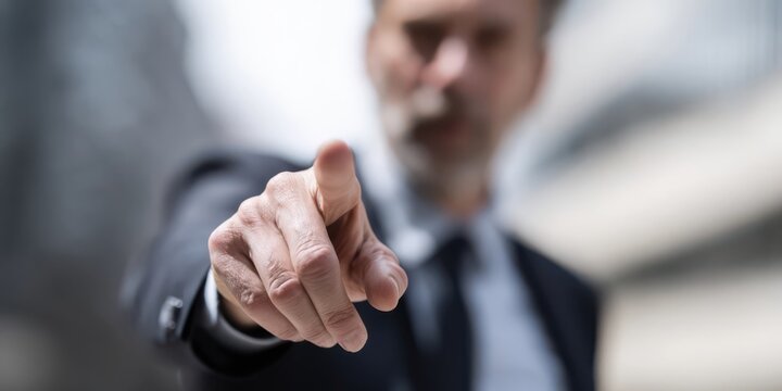 Businessman pointing directly at camera with assertive expression conveying authority, order, leadership, or confrontation.