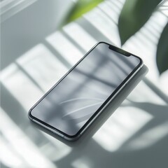 Sleek smartphone on sunlit surface with leaf shadows