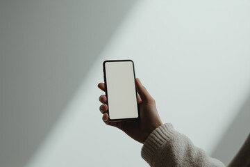 Hand holding smartphone against minimalist background in soft light