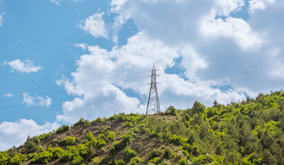 Power line tower on green hill under cloudy sky. This scene captures the intersection of nature and infrastructure. Use for themes related to energy and landscape.