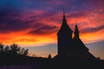 A church with a steeple and a cross on top. The sky is orange and the sun is setting