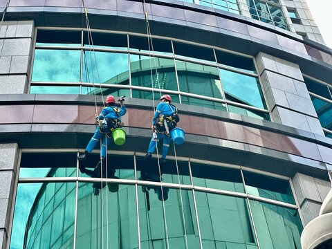 Two workers climbing to clean glass windows — a high-rise maintenance task that highlights the skill and risk involved in urban building upkeep. Tanah Abang, Jakarta - June 16, 2025 - Powered by Adobe