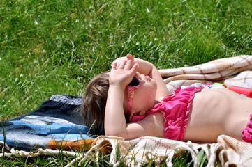 Littlegirl enjoying a sunny day lying on a blanket in the grass while shielding eyes from bright...