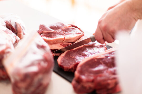 person using knife cutting beef steaks up for storage