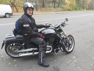 A man is sitting on a black motorcycle. He is wearing a helmet and a black jacket. The motorcycle...