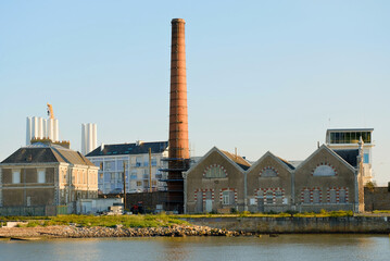 Historic Industrial Buildings and Brick Chimney with Wind Turbine Towers in Background at Sunset