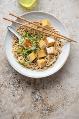 Ramen with marinated egg, smoked tofu and spring onion, vertical shot on a beige granite background with space, flat lay