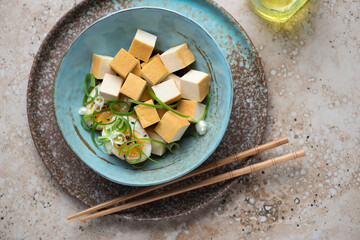 Smoked tofu cheese with marinated eggs in a turquoise bowl, horizontal shot on a beige granite background, top view