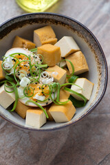 Bowl with smoked tofu cheese, soy-marinated egg and spring onion, vertical shot on a brown granite background, middle closeup