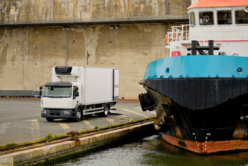 Refrigerated Delivery Truck Next to Docked Offshore Tug Supply Vessel in Industrial Port Area,...