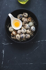 Bowl with raw fresh quail eggs on a black marble background, vertical shot, copy space, top view
