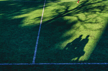 A soccer field with a shadow of two people on the grass. The shadow is on the grass and the people are not visible