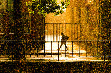 A person is walking on a sidewalk in the rain. The person is wearing a backpack