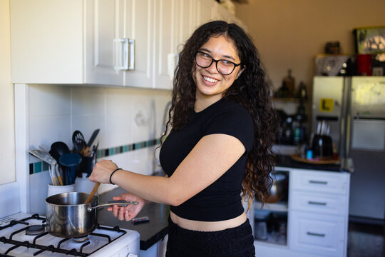 teenager wearing black stirring a saucepan in the kitchen