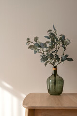 Green vase with olive plant branch on wooden table top, on neutral beige plaster wall background...
