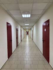 Long corridor with identical doors on each side. Symmetrical of hallway view indoors office building