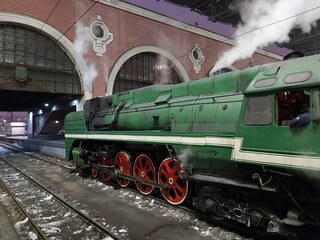 Green steam engine train with red wheels is sitting on the tracks. The train is labeled with the...
