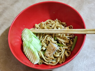 A bowl of chicken noodles with fresh cucumber slices, tofu pieces and celery sticks, served with...